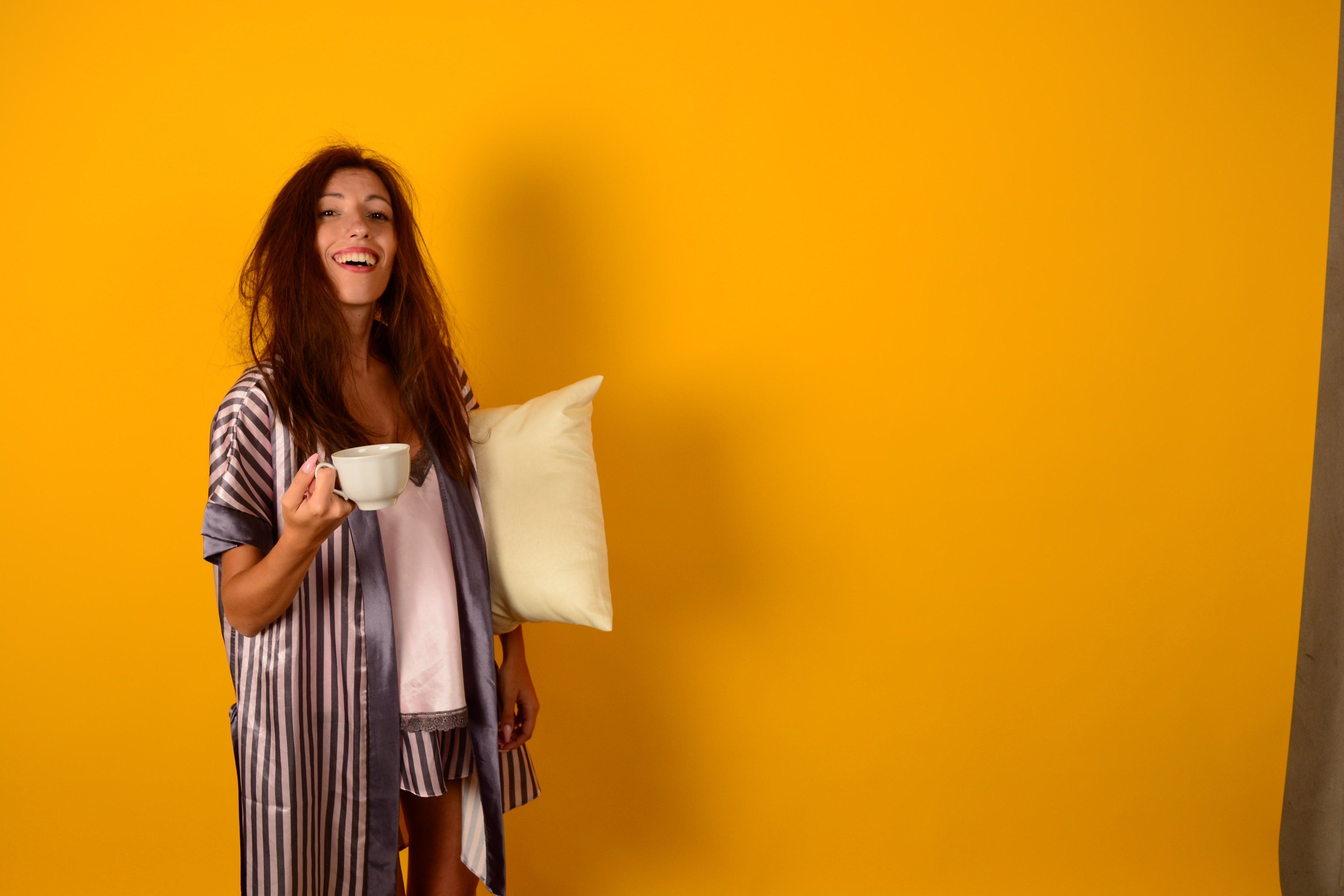 Woman holding cup and pillow in pajamas
